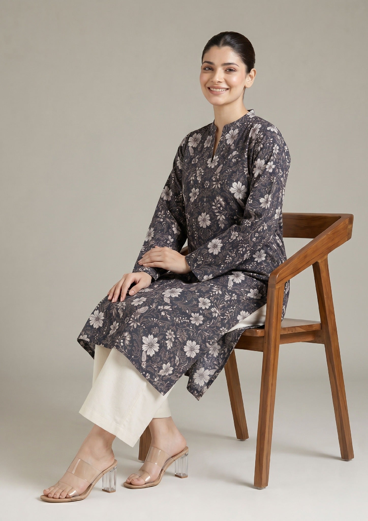Seated model wearing Evening Meadow 2 piece printed lawn co-ord set by Mirasl with charcoal floral shirt, off-white trouser, and summer ready styling.