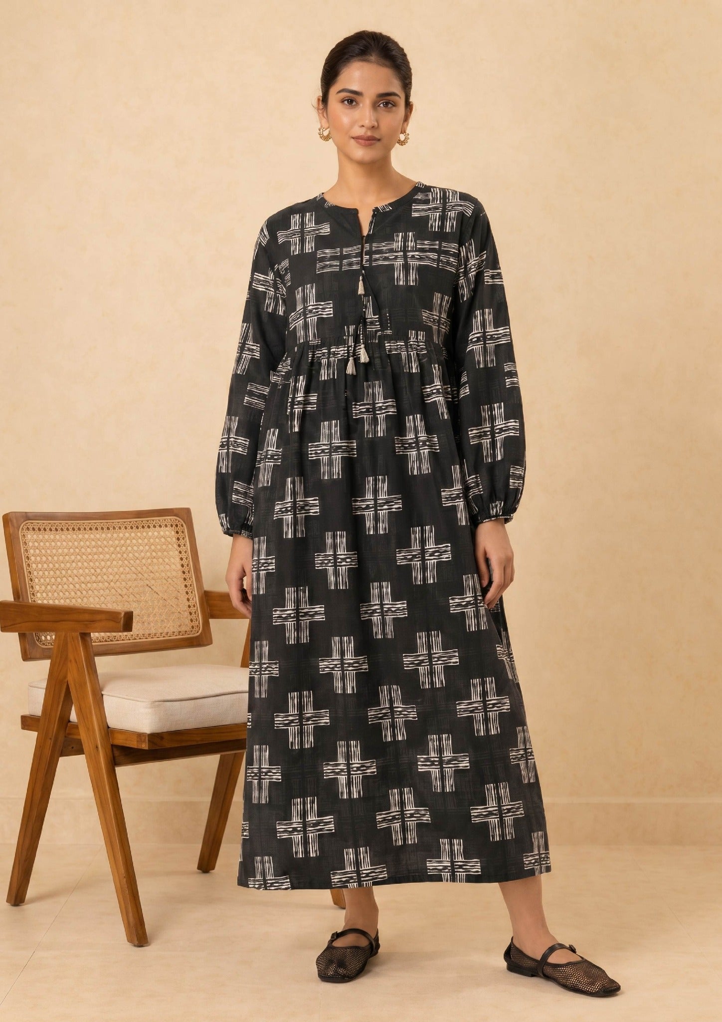 Seated model wearing Ebony Crossroad by Mirasl, an ebony black printed lawn co-ord set with off-white cross motifs, tassel neckline, gathered waist detail, and relaxed breathable fit.