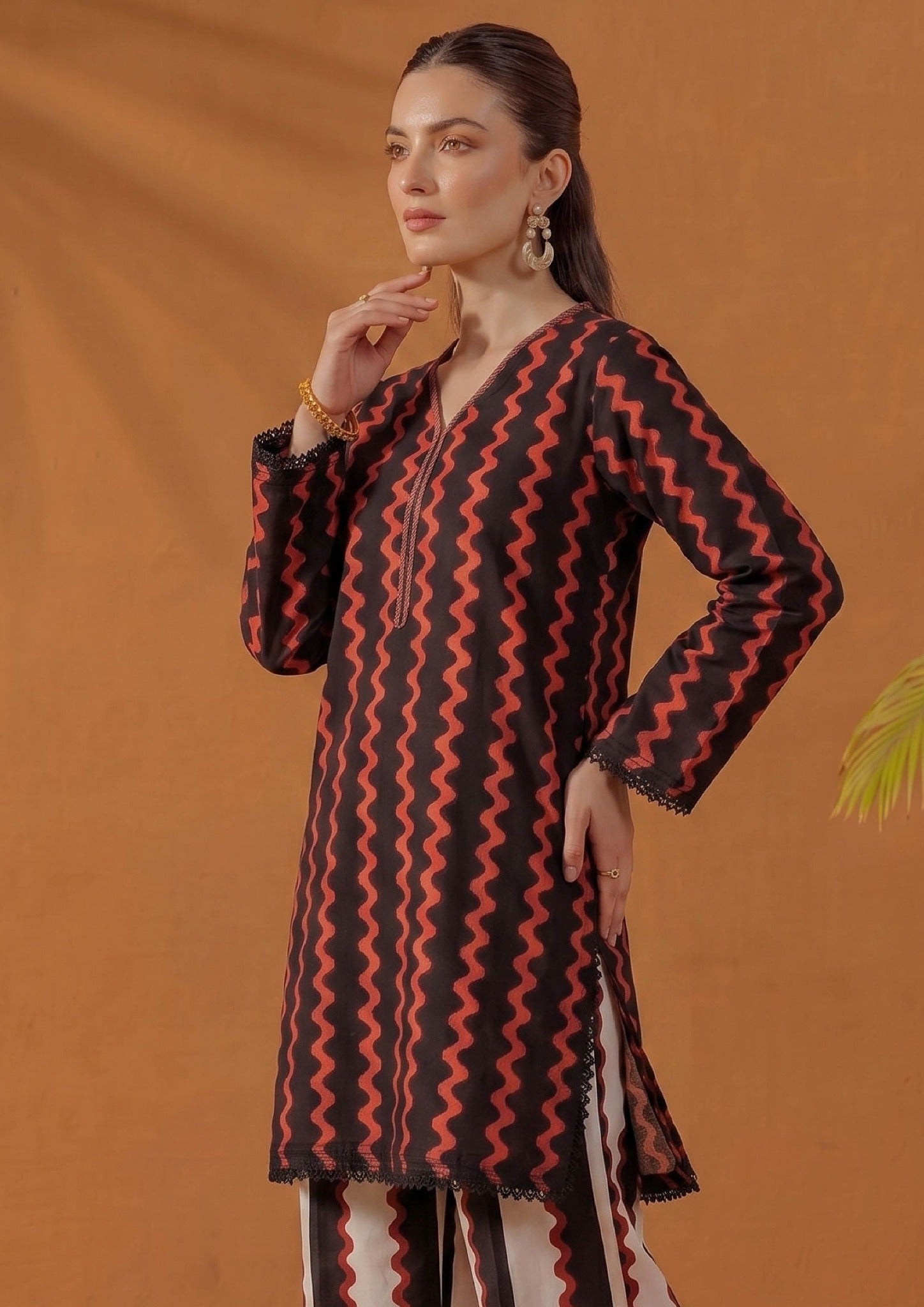 Seated model wearing Crimson Ripple by Mirasl, a black and crimson red printed lawn co-ord set with ripple print shirt, coordinated stripe trouser, lace finishing, and summer ready styling.