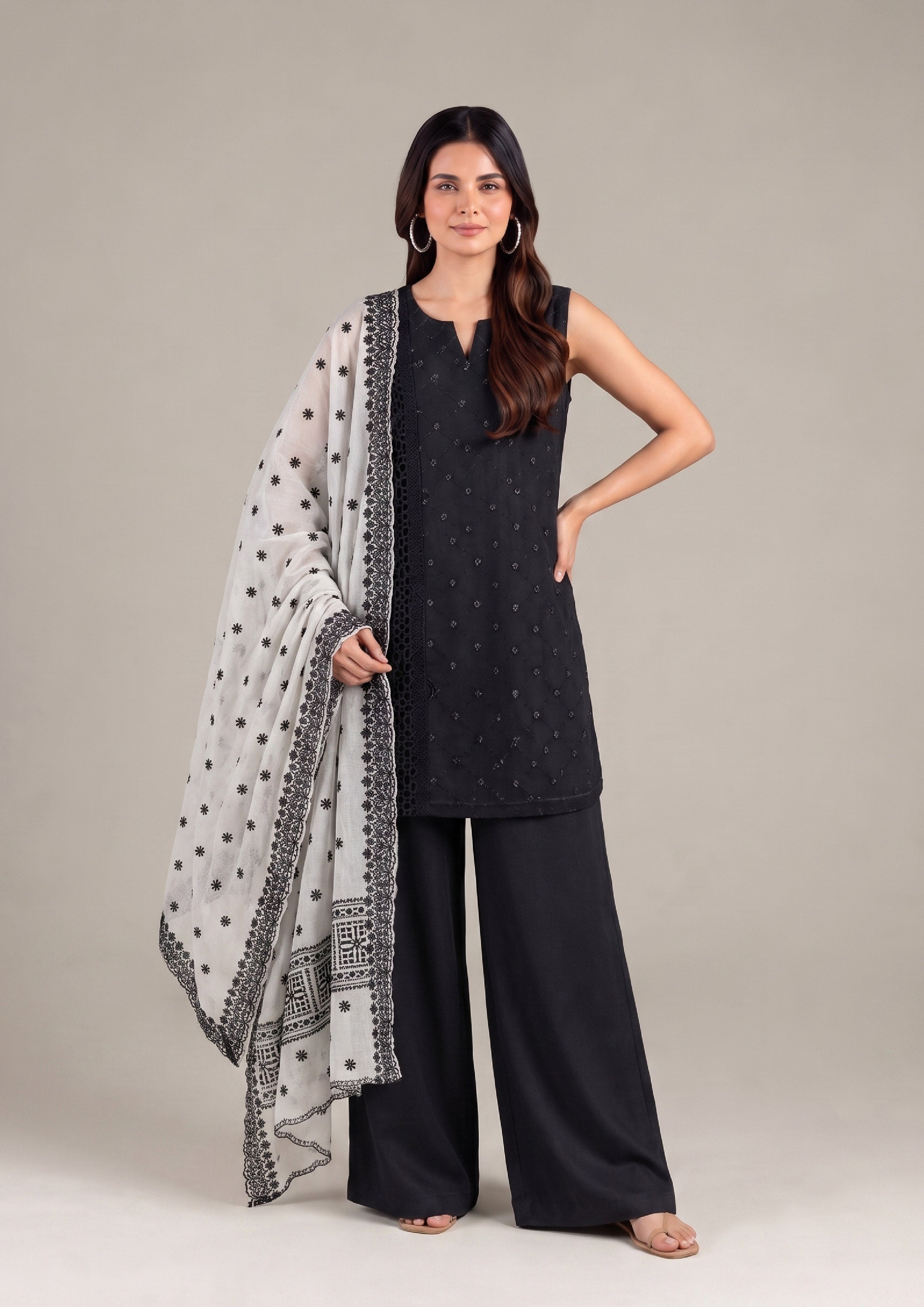 Full-length front view of a woman wearing a black embroidered sleeveless kurta, black palazzo trousers, and a white embroidered dupatta.