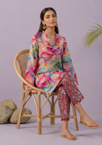 Seated model wearing Mirasl Blossom Bramble stitched lawn 2 piece co-ord set with vibrant floral printed shirt and printed straight trouser.