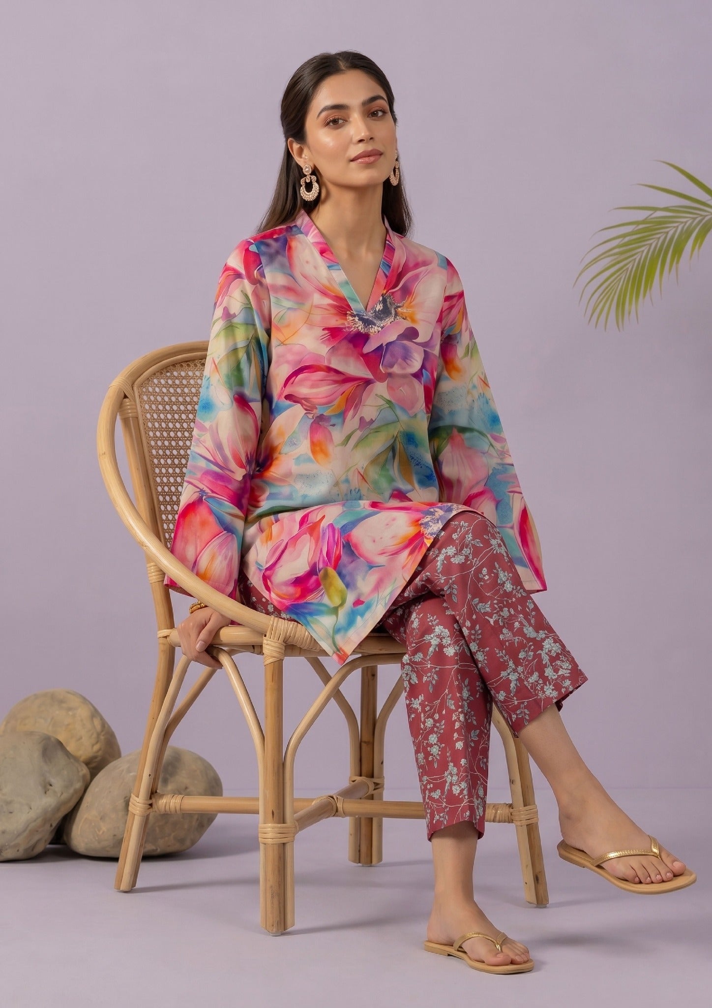 Seated model wearing Mirasl Blossom Bramble stitched lawn 2 piece co-ord set with vibrant floral printed shirt and printed straight trouser.
