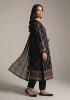 Seated model wearing Crimson Mosaic Noir black designer lawn suit with pearl earrings and patterned dupatta