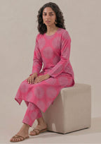 Seated model wearing Mirasl Fuchsia Mandala 2 piece co-ord set with fuchsia pink printed lawn knee-level shirt and matching straight trouser.