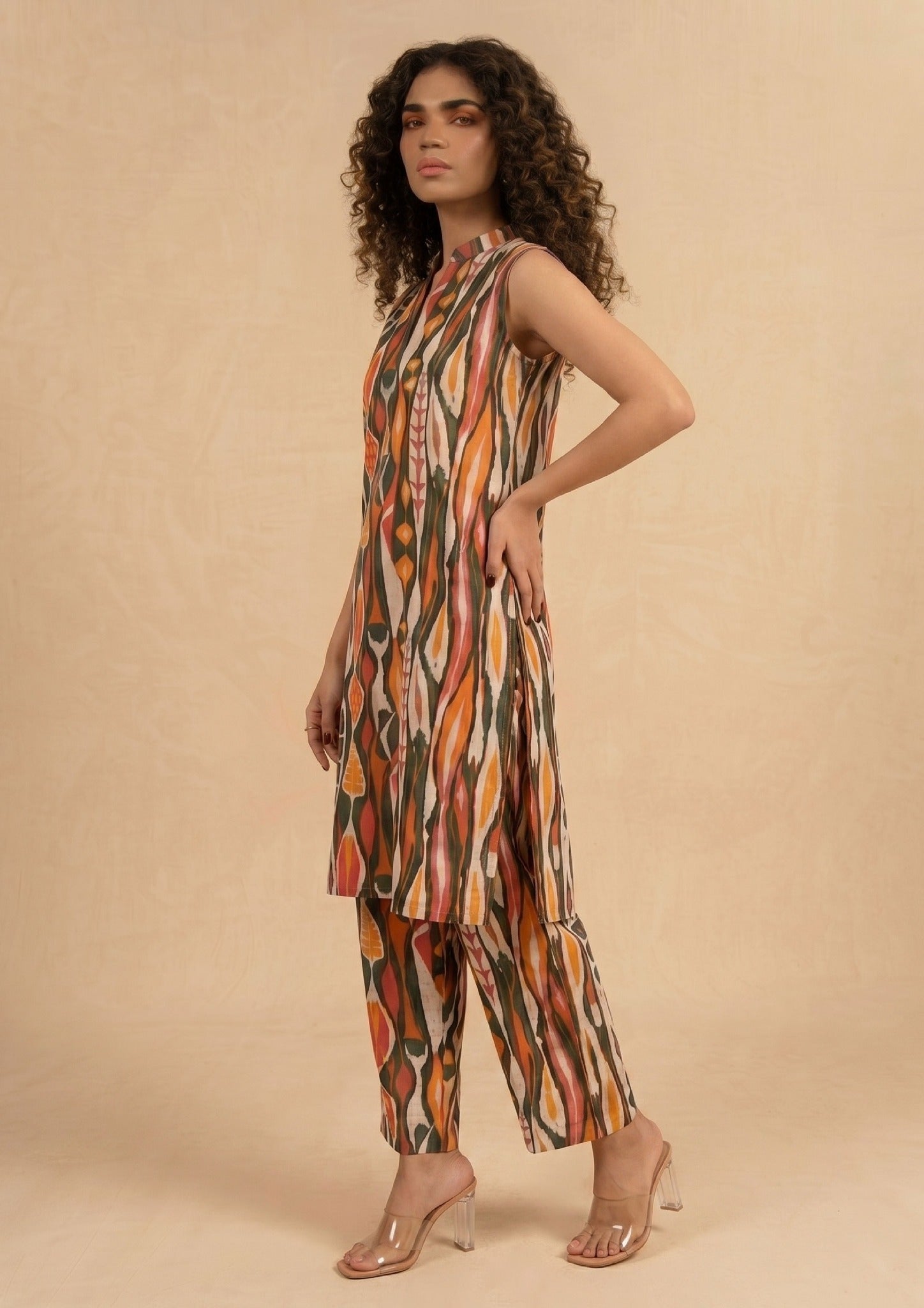 Standing view of Linear Illusion by Mirasl featuring an earthy printed lawn outfit with orange, rust, olive, coral, and dark green linear motifs.