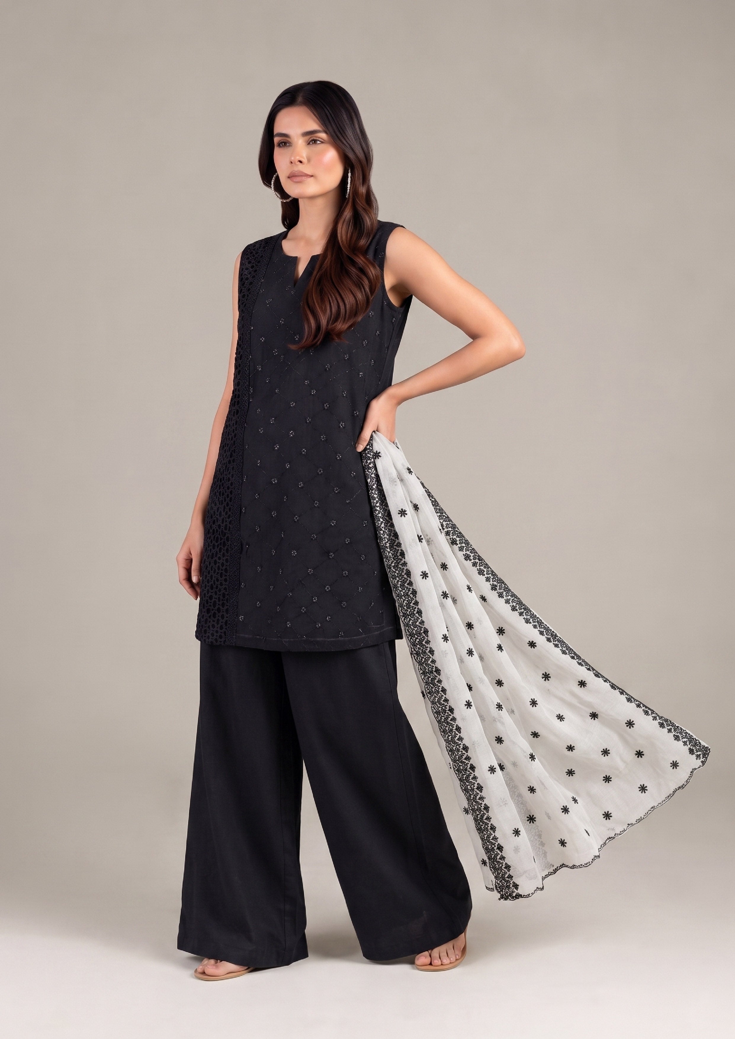 Fashion model posing in a modern black sleeveless embroidered kurta with wide-leg palazzo pants and flowing white embroidered dupatta.
