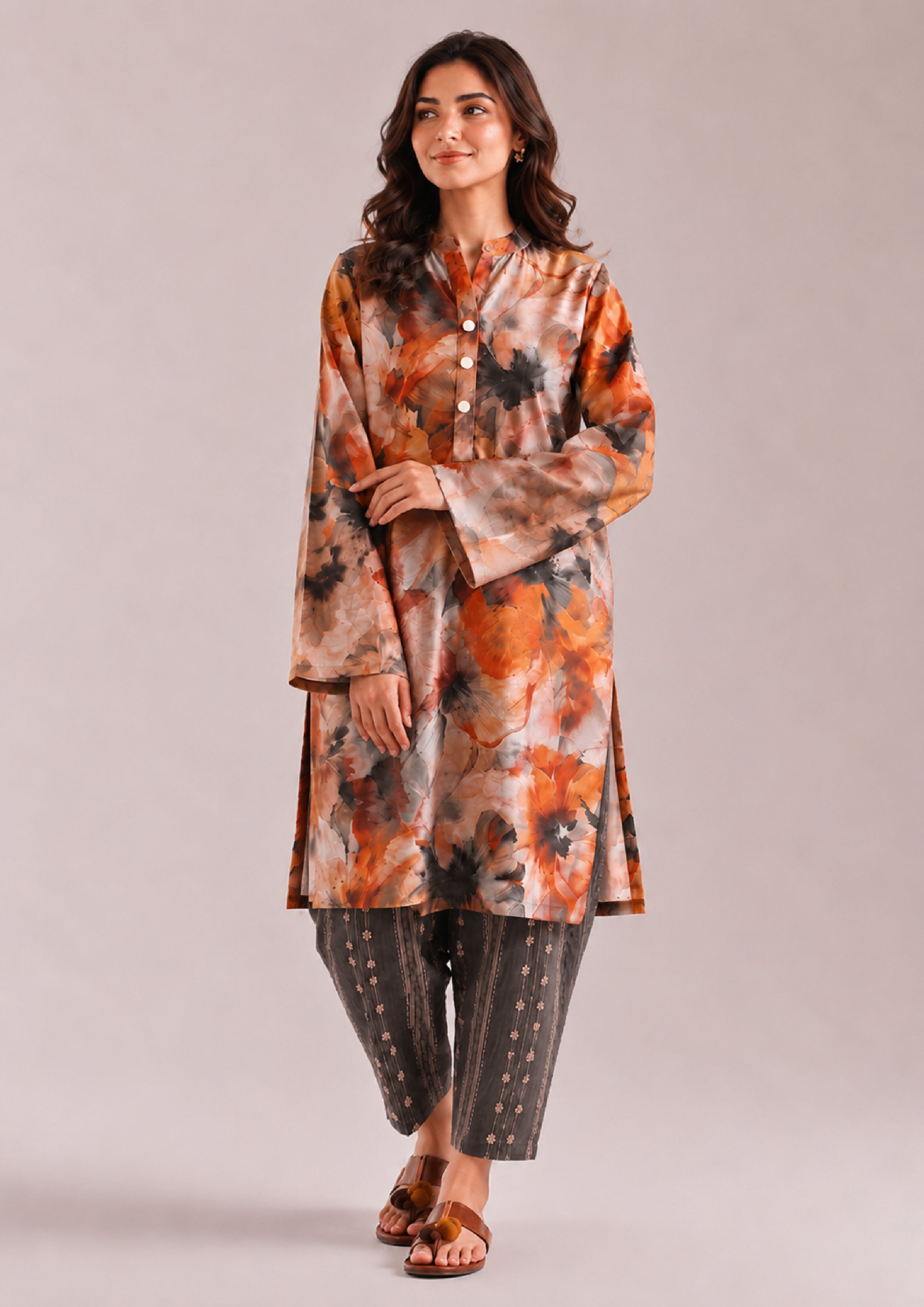 Front walking pose of a women's Printed Lawn Suit with an orange, beige and charcoal grey floral print shirt paired with striped grey trousers from the Fasl-e-Rang collection by Mirasl.