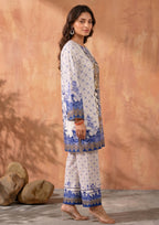 Seated model wearing Mirasl Ornate Ocean printed lawn co-ord set with ornate blue floral shirt, border sleeves, and matching printed straight trouser.