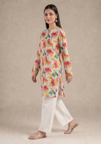 Seated model wearing Petal Radiance 2 piece printed lawn co-ord set by Mirasl with floral printed knee-level shirt and white trouser.