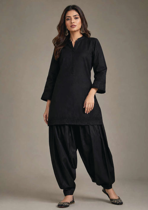 Front full look of Pleated Afghani Noir black 2 piece coard suit with pleated long shirt, band collar and voluminous Afghani shalwar