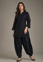 Front standing view of Pleated Afghani Noir Afghani shalwar suit with black pleated shirt, band collar and relaxed draped shalwar