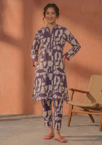 Seated model wearing Plum Mosaic 2 piece printed lawn co-ord set by Mirasl with abstract printed knee-level shirt, straight trouser, and summer ready styling.